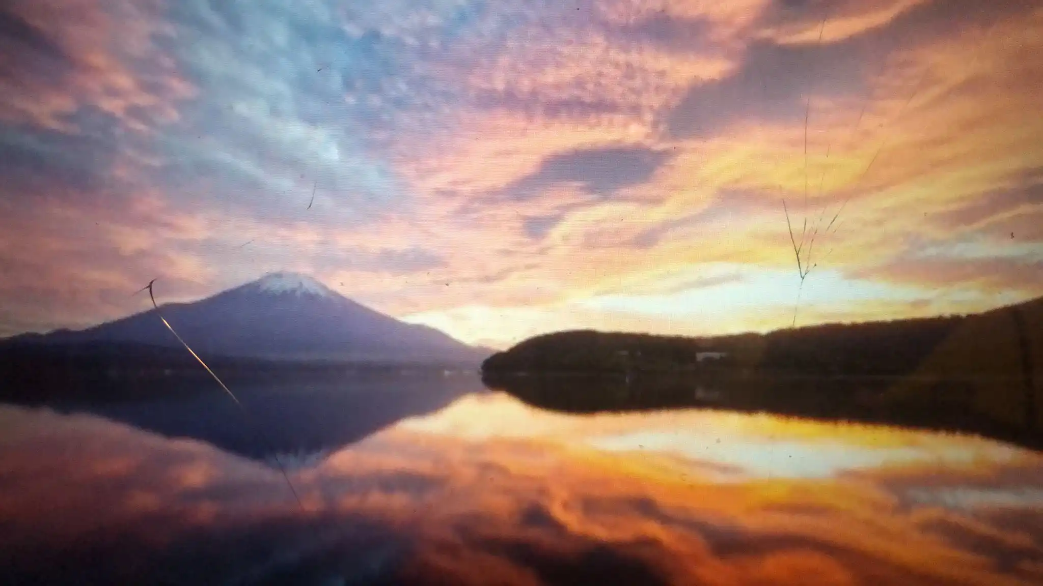 großer See mit einem Wald und Berg im Hintergrund, bei aufgehender Sonne